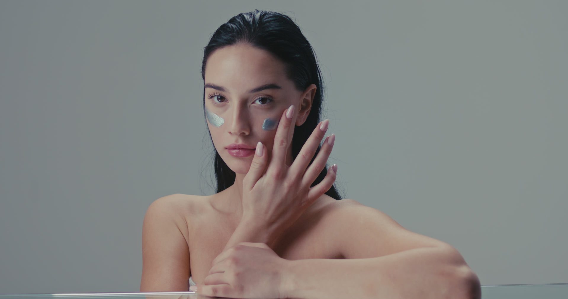 Porträt einer Frau mit feuchtigkeitsspendender Creme im Gesicht, die direkt in die Kamera blickt – modernes Skincare-Ritual in minimalistischer Ästhetik.